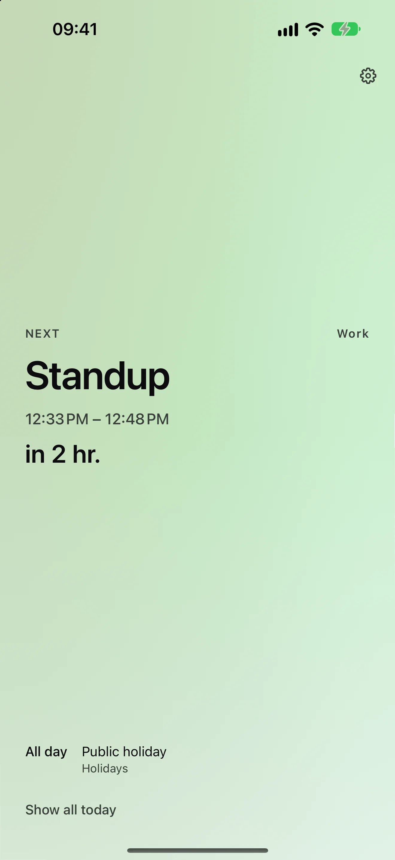 Upnext in light mode on a pale green field: the hero shows the next timed event, Standup, with the countdown “in 2 hr.”, while an all-day Public holiday sits in the rail underneath labelled All day — the holiday never takes over the hero.