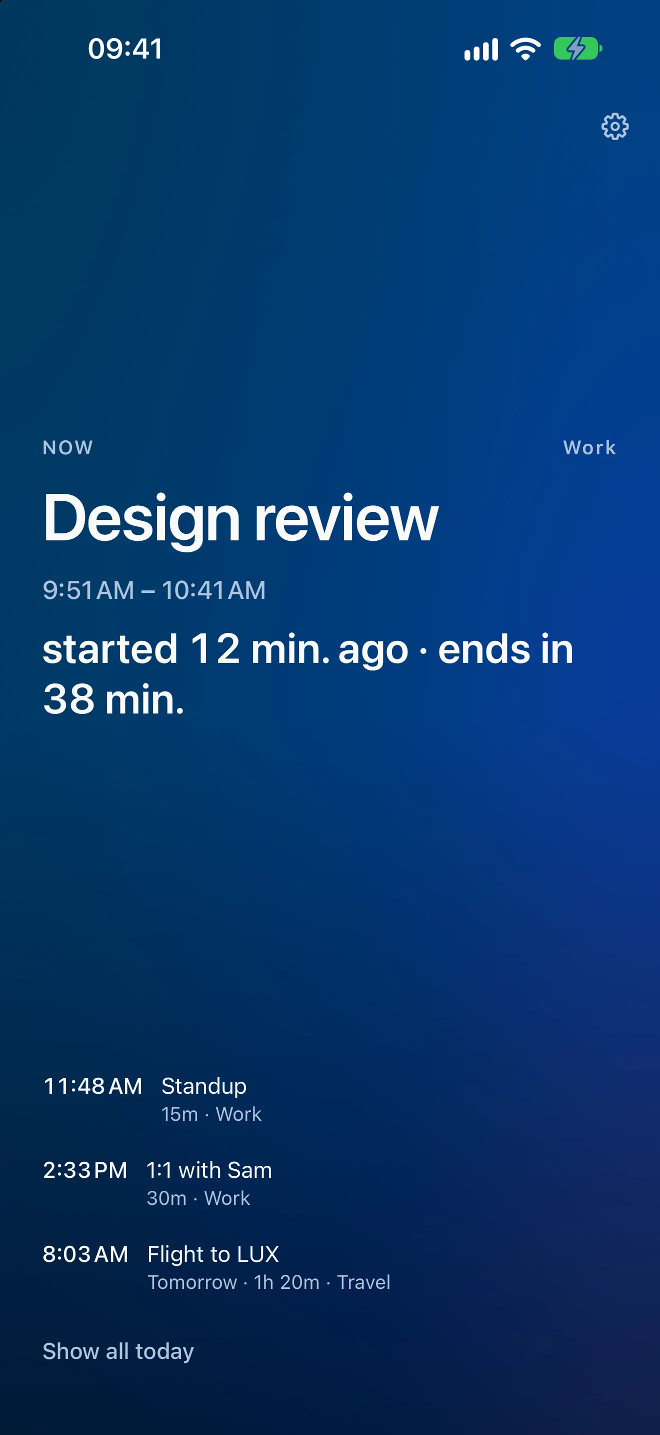 Upnext on iPhone in dark mode showing an event in progress: a deep blue field with the word NOW and the calendar name Work above a large white title reading “Design review”, the time range 9:51 AM – 10:41 AM beneath it, and a countdown reading “started 12 min. ago · ends in 38 min.” Three upcoming events sit at the bottom — Standup, 1:1 with Sam and a flight tomorrow — with a Show all today button under them.